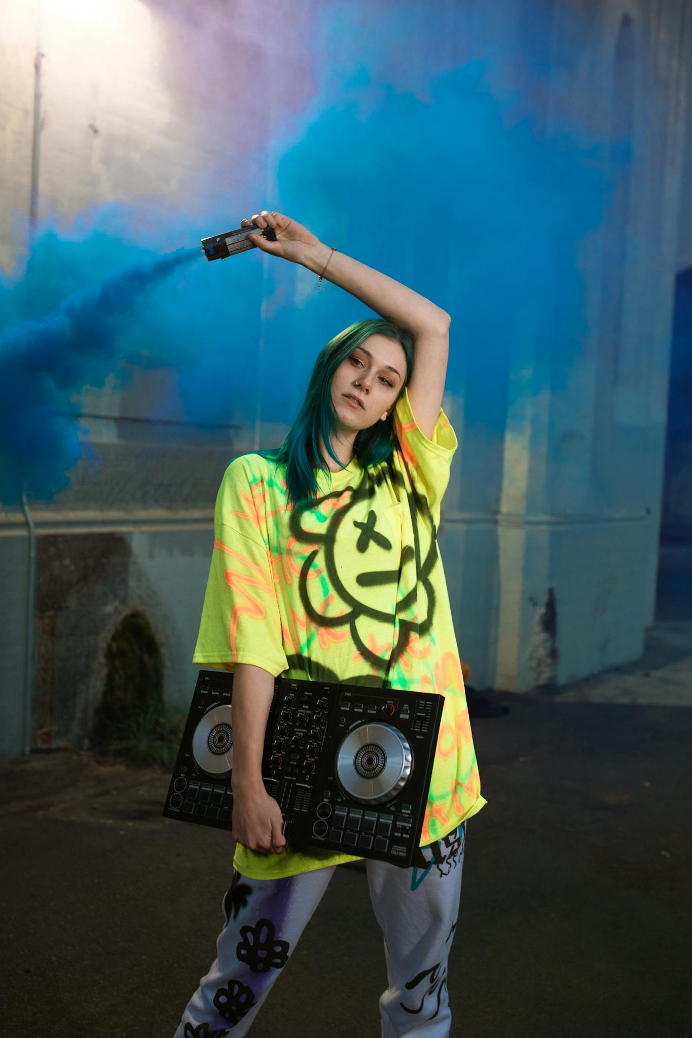 DJ in vibrant streetwear holding DJ controller and smoke bomb for a trendy, urban scene.